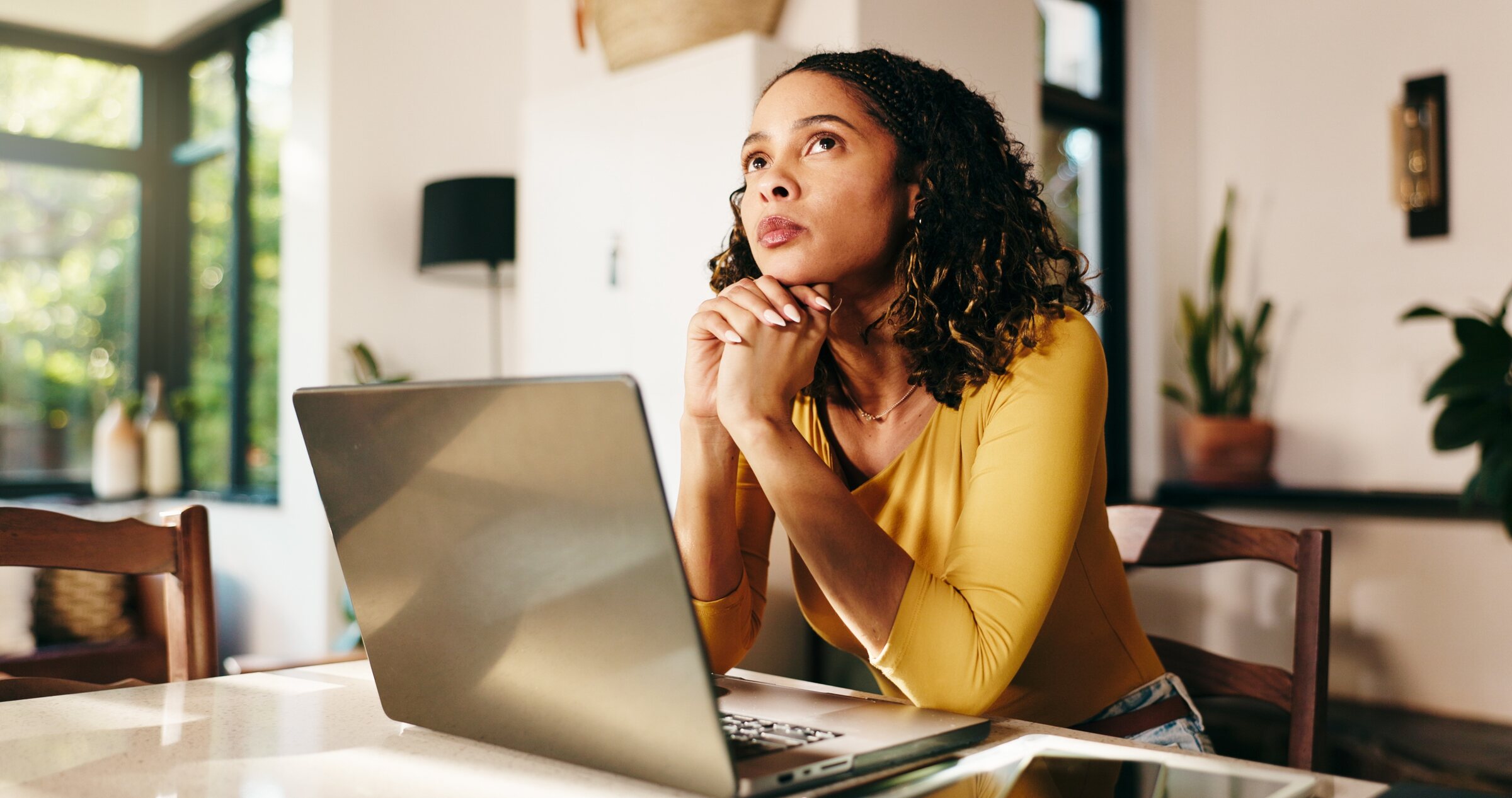 A woman sits at her laptop, thinking